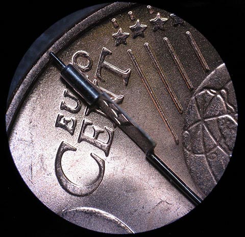 Antike Tischuhr mit Spindelhemmung. Herstellung der Unruhwelle. In der polierten Palette der Unruhwelle spiegeln sich die Buchstaben einer Münze.